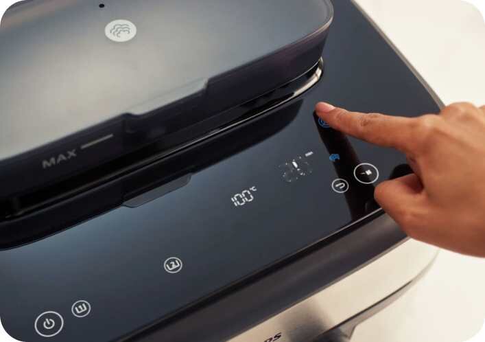 Zbliżenie na panel dotykowy frytkownicy beztłuszczowej z wyświetlaczem pokazującym temperaturę 100°C. Widoczna jest ręka dotykająca przycisk na panelu.