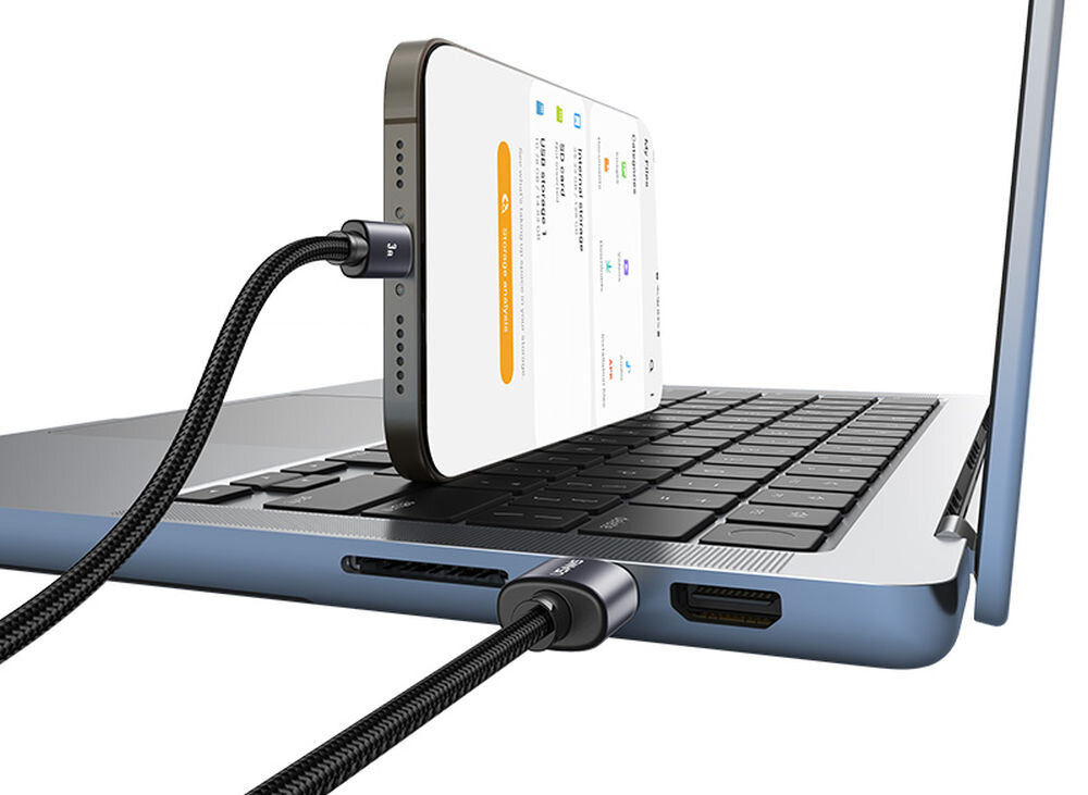 Na obrazie widać laptopa z podłączonym smartfonem za pomocą metalicznego kabla USB-C - USB-A. Kabel jest wpięty do portu USB laptopa, a smartfon jest ustawiony pionowo na klawiaturze.