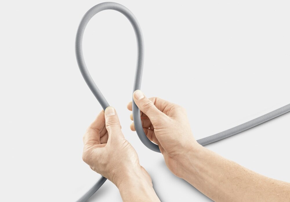 Dwie dłonie trzymają szary wąż ogrodowy uformowany w pętlę. Tło jest jednolite i jasne.