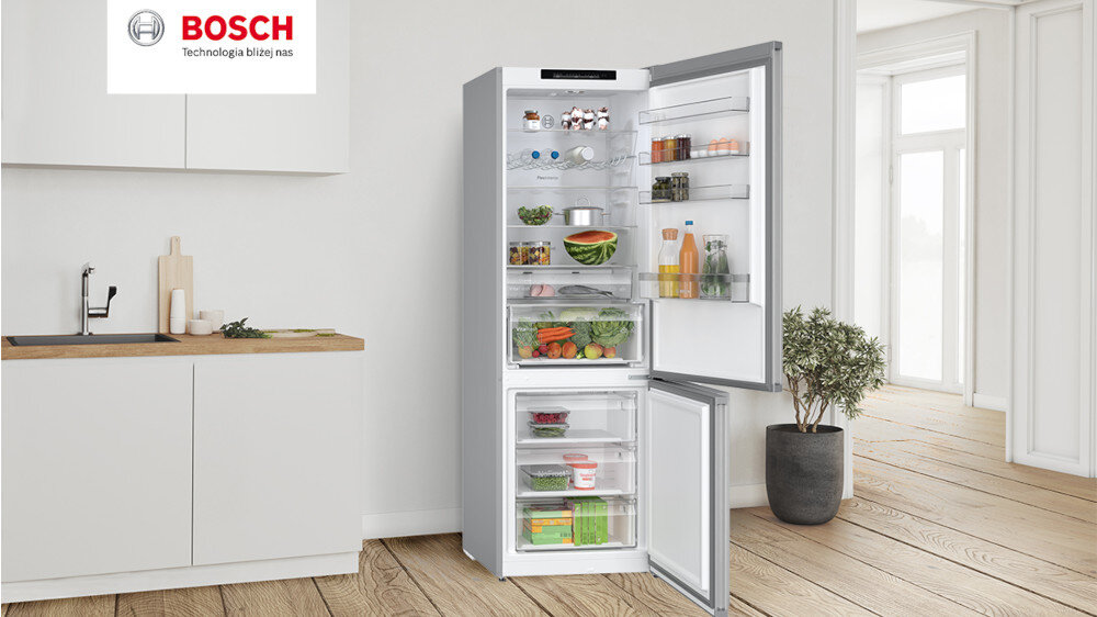 Otwarta lodówka w kuchni, wypełniona różnorodnymi produktami spożywczymi, takimi jak owoce, warzywa i napoje. Na górze obrazu widoczne jest logo BOSCH z napisem \'Technologia bliżej nas\'.