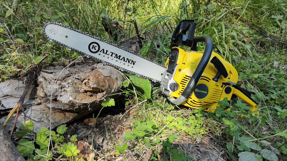 Żółta piła spalinowa leży na trawie obok ściętego pnia drzewa. Na prowadnicy widoczny jest napis \'KALTMANN\'.