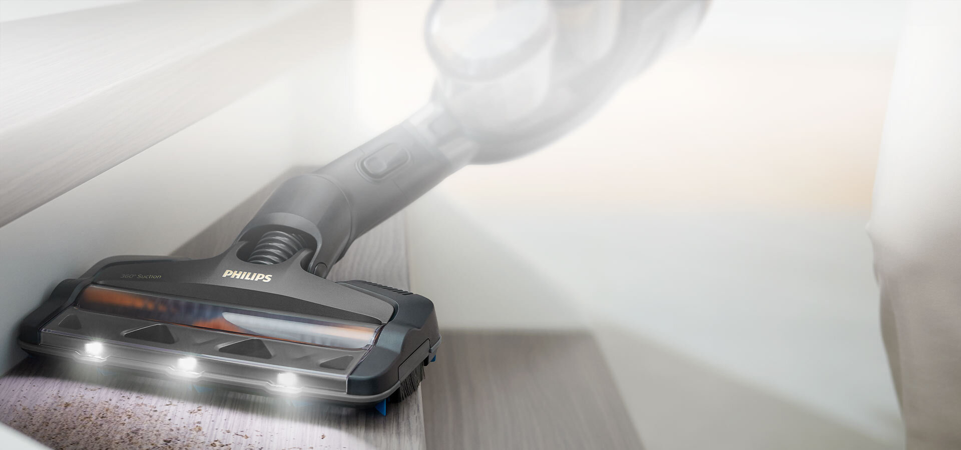Odkurzacz z logo Philips odkurza schody, emitując światło z trzech diod LED. Na powierzchni widoczne są drobinki kurzu.