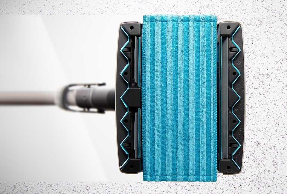 Na obrazie widoczna jest głowica odkurzacza z niebieską, prążkowaną nakładką mopującą. Tło jest jasne i jednolite.