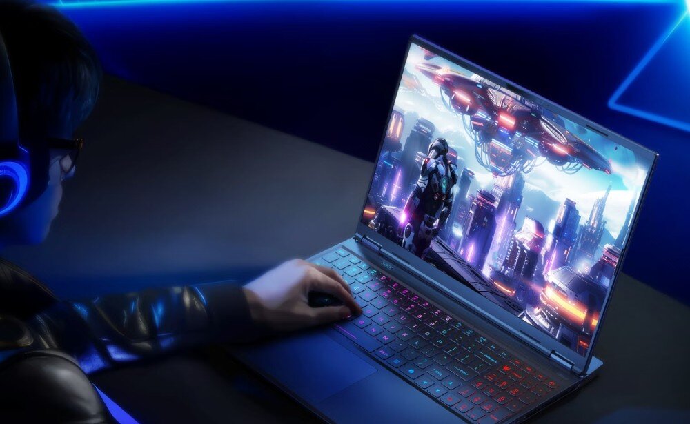 Osoba używa laptopa z kolorową klawiaturą, na ekranie widoczna jest scena z gry komputerowej przedstawiająca futurystyczne miasto i postać w zbroi. W tle widać niebieskie światła i elementy dekoracyjne.