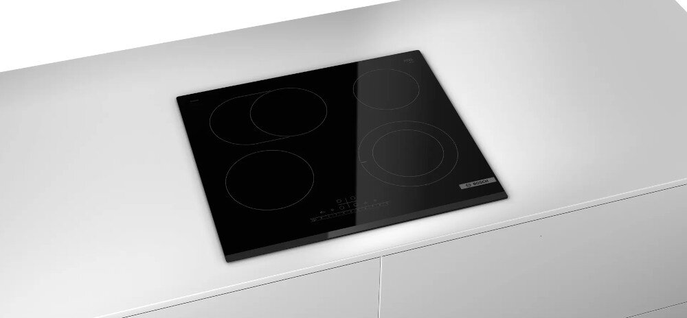Czarna płyta ceramiczna z czterema okrągłymi polami grzewczymi, zamontowana na białym blacie. Widoczne jest logo producenta oraz panel dotykowy z oznaczeniami funkcji.