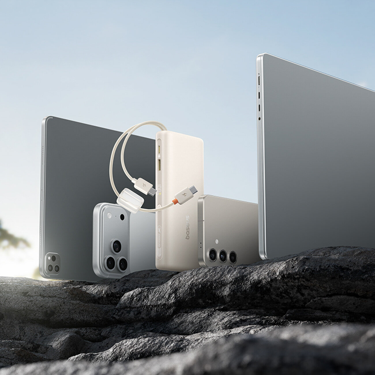 Na obrazie widoczny jest powerbank z wbudowanymi kablami USB-C, otoczony przez różne urządzenia elektroniczne. Na powerbanku znajduje się napis \'Baseus\'.