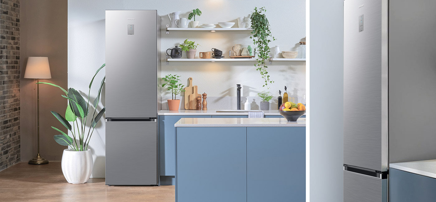 Ponadczasowe wykończenie lodówki w kolorze szczotkowanej stali nierdzewnej Kuchnia z lodówką w kolorze szczotkowanej stali nierdzewnej, obok której znajduje się roślina w białej donicy. Na blacie kuchennym stoją różne naczynia i dekoracje, a na ścianie wiszą półki z dodatkowymi przedmiotami.