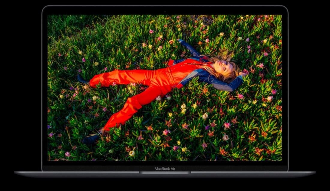 Laptop z wyświetlaczem pokazującym osobę leżącą na trawie w kolorowym ubraniu. Na obudowie widoczny jest napis \'MacBook Air\'.