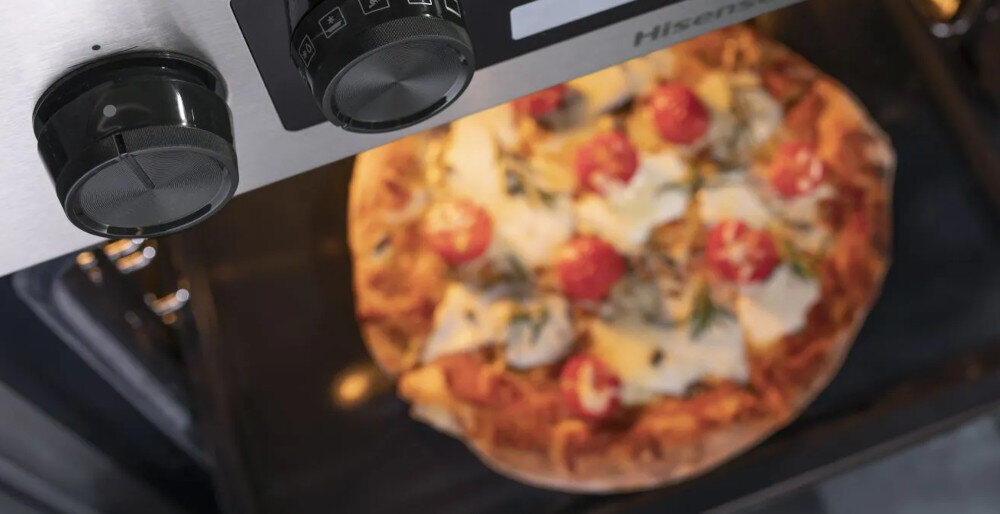 Zbliżenie na wnętrze piekarnika z widoczną pizzą na ruszcie. Na panelu sterowania widoczne są dwa pokrętła oraz logo \'Hisense\'.