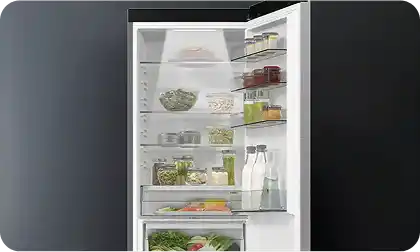 Otwarta lodówka z widocznymi półkami, na których znajdują się różne produkty spożywcze, takie jak warzywa, słoiki i butelki. Wnętrze jest dobrze oświetlone, a drzwi lodówki mają dodatkowe półki na mniejsze przedmioty.