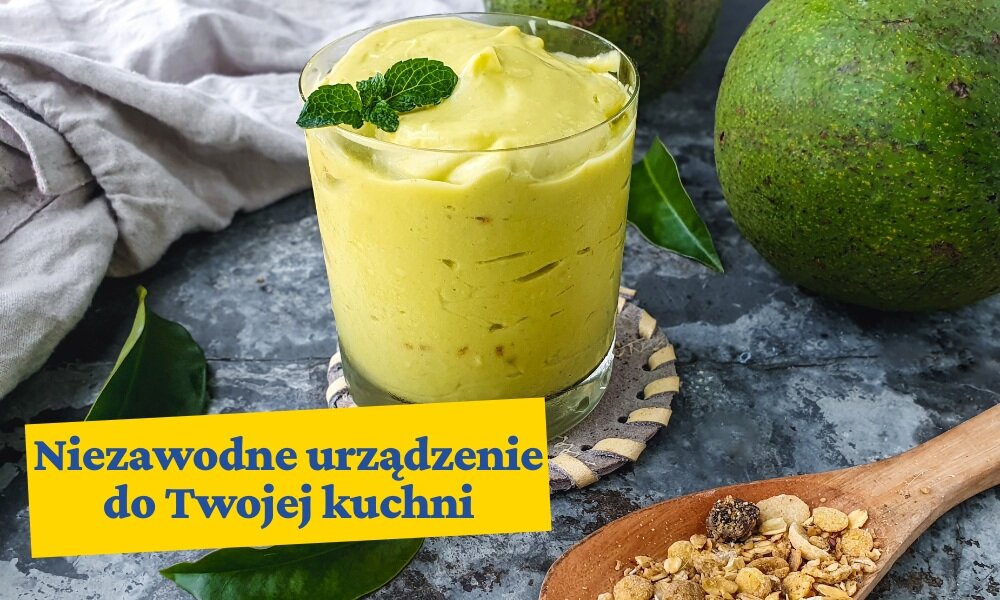 Na obrazie znajduje się szklanka z zielonym smoothie ozdobionym listkiem mięty, obok leży drewniana łyżka z musli. Na dole widoczny jest napis: \'Niezawodne urządzenie do Twojej kuchni\'.