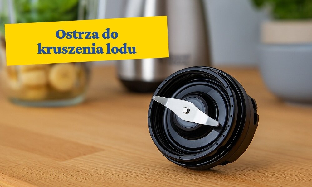 Na drewnianym blacie znajduje się czarny element z ostrzem, prawdopodobnie część blendera. W tle widoczny jest napis na żółtym tle: \'Ostrza do kruszenia lodu\'.