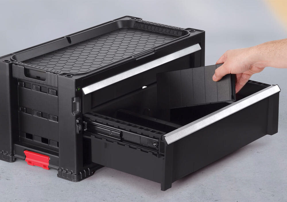 Regał z szufladami KETER 17201228 Czarny podłoga część regału ustawiona na podłodze otwarta szuflada osoba wyciąga z niej przegródkę elementy solidnie zespolone płynne działanie szuflad komfort pracy porządek bezpieczeństwo