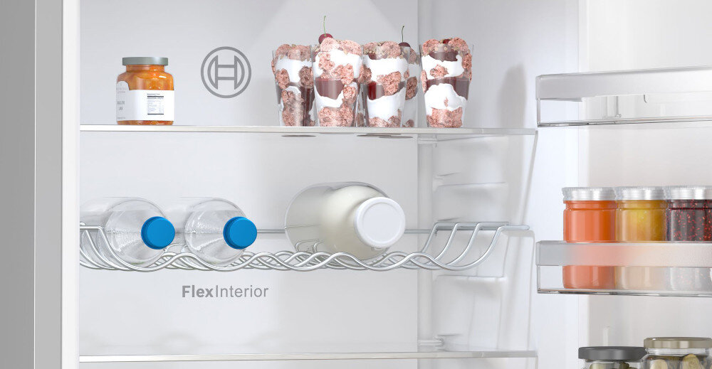 Wnętrze lodówki z widocznymi półkami, na których znajdują się słoiki, butelki i pojemniki z jedzeniem. Na jednej z półek widoczny jest napis \'FlexInterior\' oraz logo producenta.