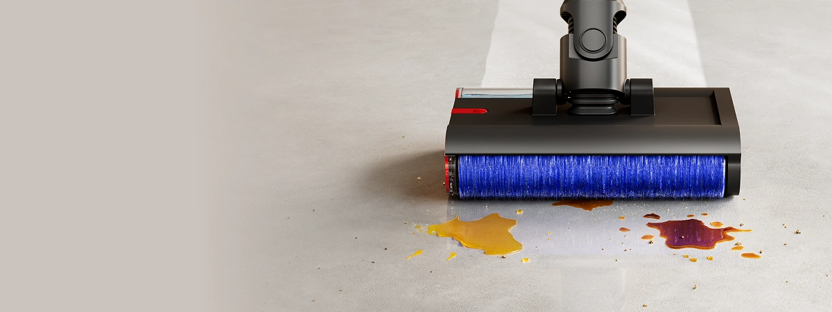 Na obrazie widać elektryczny mop z niebieską szczotką, który czyści rozlane płyny na podłodze. Mop jest bezprzewodowy i ma ciemną obudowę.