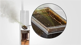 Obraz przedstawia zbliżenie na filtr zanieczyszczony brązowym osadem, umieszczony w urządzeniu czyszczącym. W tle widoczna jest para wydobywająca się z urządzenia.