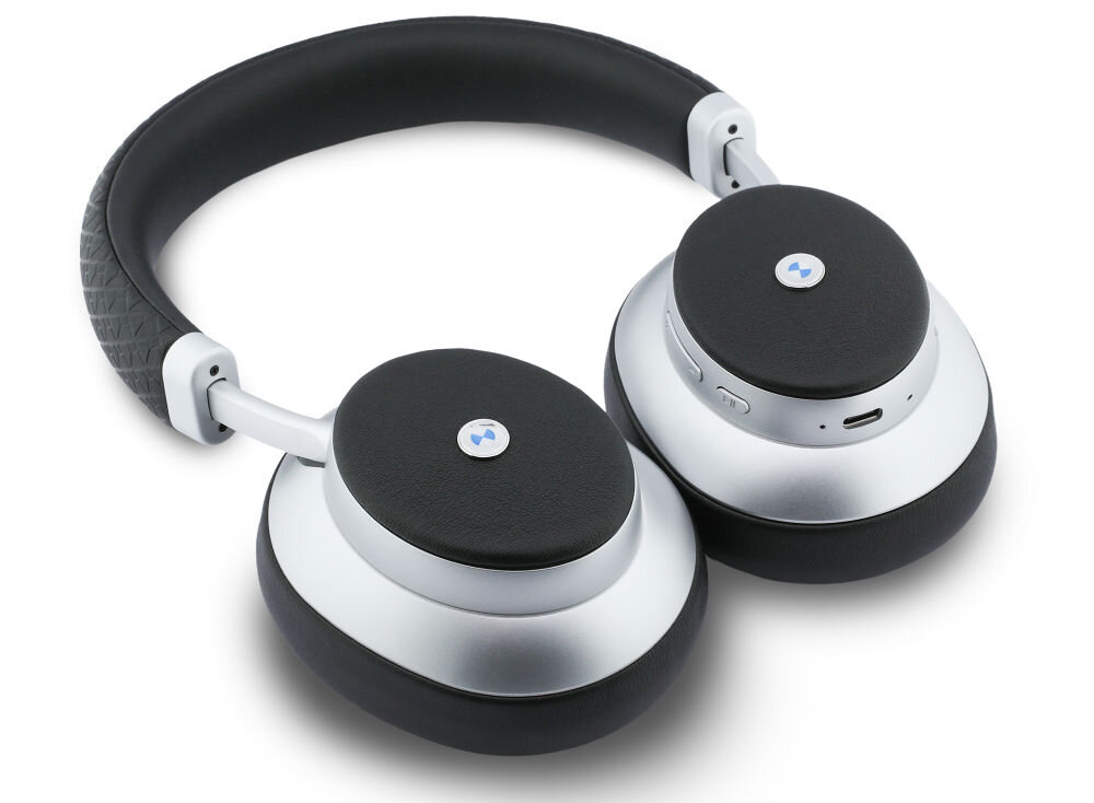 Srebrne słuchawki nauszne z czarnymi poduszkami i metalowym logo na zewnętrznej stronie muszli. Na jednej z muszli widoczne są przyciski sterujące oraz port ładowania.