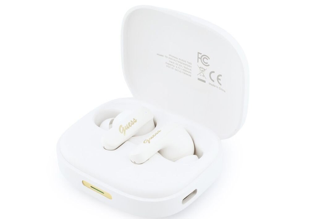 Białe słuchawki douszne z logo \'Guess\' w złotym kolorze umieszczone w otwartym etui ładującym. Na wewnętrznej stronie pokrywy etui widoczne są oznaczenia certyfikacyjne oraz napis \'Made in China\'.