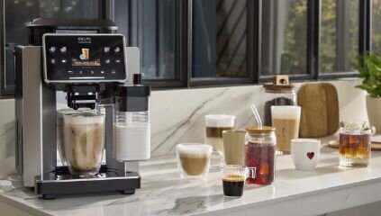 Ekspres do kawy KRUPS na blacie, obok różne kawy w szklankach.