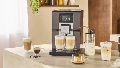 Ekspres do kawy KRUPS  na blacie, robi kawę do dwóch filiżanek. Obok kilka szklanek z różną kawą.