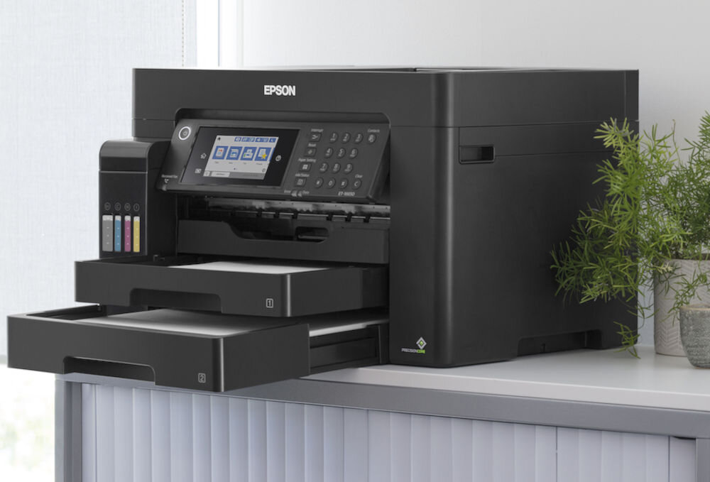 Urządzenie wielofunkcyjne EPSON EcoTank L15150 Druk w kolorze, Automatyczny druk dwustronny, Wi-Fi prezentacja urządzenia na szafce obok kawiatek jasna ściana wydajność atramentu wydłużenie czasu pracy