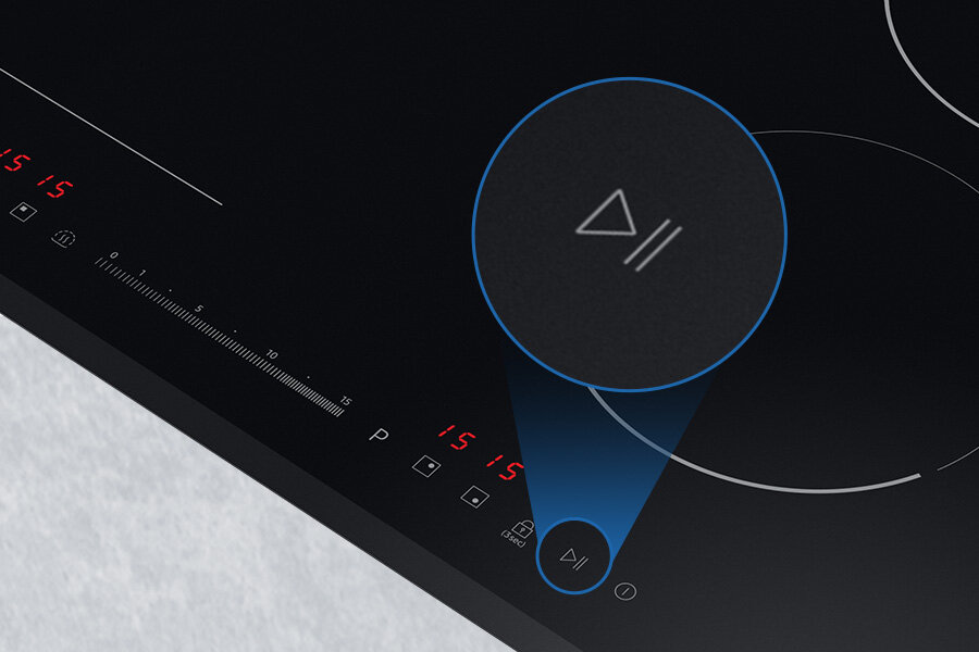 Czarna płyta indukcyjna z dotykowym panelem sterowania, na którym widoczne są cyfry \'15\' oraz symbole. W centralnej części znajduje się powiększony przycisk z symbolem trójkąta i dwóch pionowych linii.
