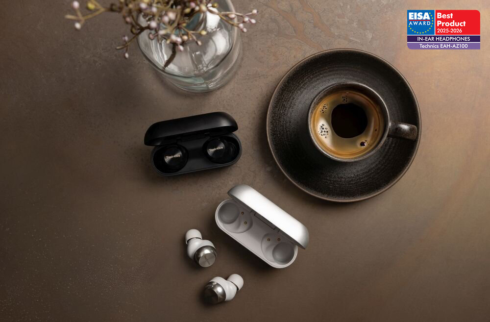 Na stole znajdują się dwa etui na słuchawki dokanałowe, jedno czarne i jedno białe, obok filiżanki kawy. W prawym górnym rogu widoczna jest plakietka z napisem: \'EISA AWARD Best Product 2023-2024 IN-EAR HEADPHONES Technics EAH-AZ100\'.