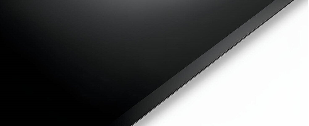 Obraz przedstawia fragment czarnej, błyszczącej powierzchni, prawdopodobnie płyty indukcyjnej, na tle białego tła. Widoczna jest krawędź urządzenia.