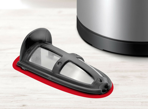 Na jasnym blacie leży czarny filtr do czajnika z metalową siatką, obok widoczna jest dolna część srebrnego urządzenia.