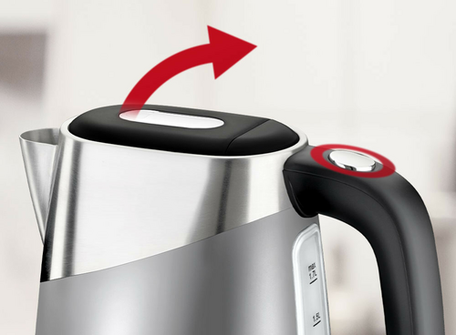 Czajnik elektryczny z metalicznym korpusem i czarną rączką, na której znajduje się przycisk. Czerwona strzałka wskazuje kierunek otwierania pokrywy.
