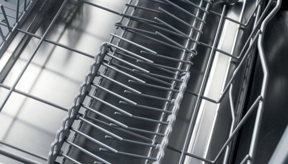 Wnętrze zmywarki z widocznymi metalowymi koszami i uchwytami na naczynia. Konstrukcja wykonana jest ze stali nierdzewnej.