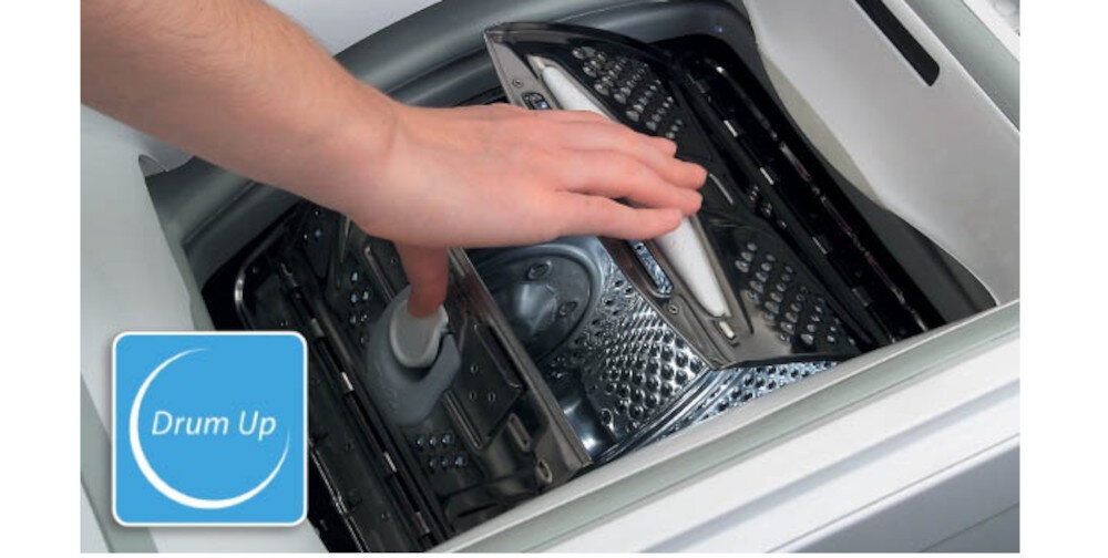 Osoba otwiera bęben pralki, widoczna jest metalowa konstrukcja wewnętrzna. W lewym dolnym rogu znajduje się niebieska ikona z napisem \'Drum Up\'.