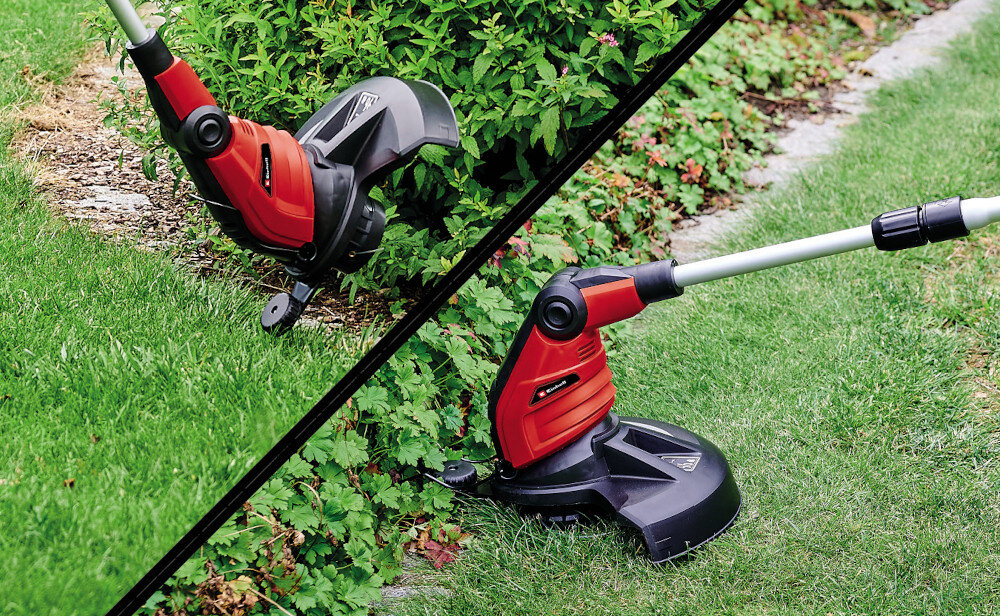 Na obrazie widoczna jest czerwona podkaszarka elektryczna używana do przycinania trawy przy krawędzi trawnika. Urządzenie ma czarną osłonę i teleskopowy uchwyt, a w tle widać zieloną trawę i krzewy.