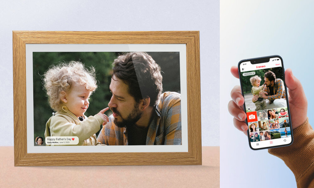 Na obrazie widoczna jest cyfrowa ramka z drewnianą obwódką, wyświetlająca zdjęcie dorosłego z dzieckiem oraz tekst \'Happy Father\'s Day, From: William, June 18, 2023\'. Obok znajduje się ręka trzymająca smartfon z aplikacją Frameo, pokazującą to samo zdjęcie i kilka miniatur innych zdjęć.